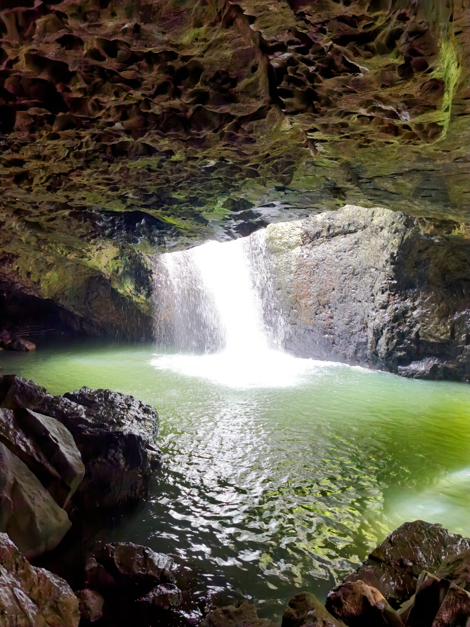 Sparkling white water cascades into a green pool at Natural Bridge